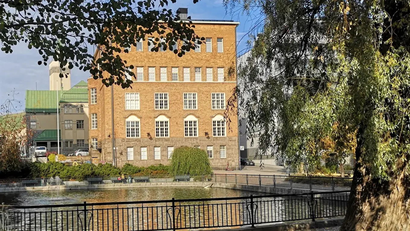 Kesäinen kuva Tampereen Monitoimitalosta, joki ja koivuja edessä